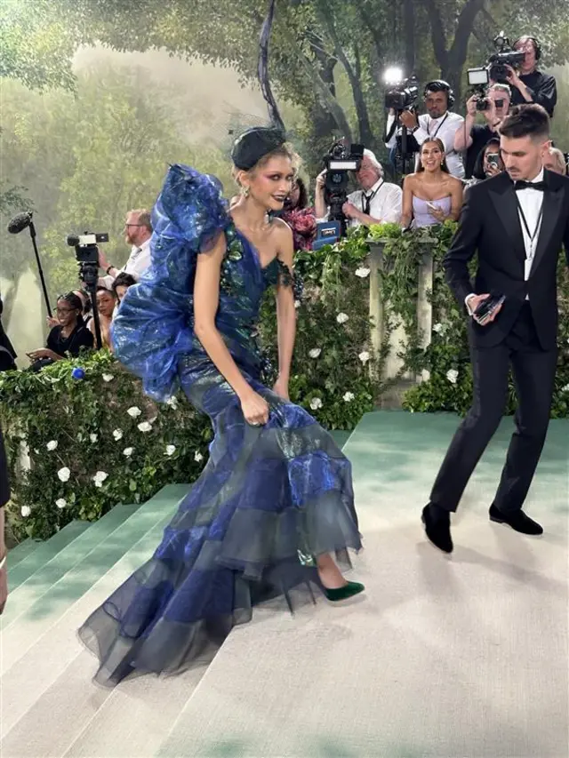 Zendaya wears a blue dress and grins as she walks up steps on the carpet