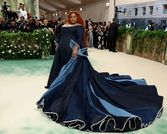 Da'Vine Joy Randolph wears a flowing gown made of different shades of blue denim with ruffled sleeves