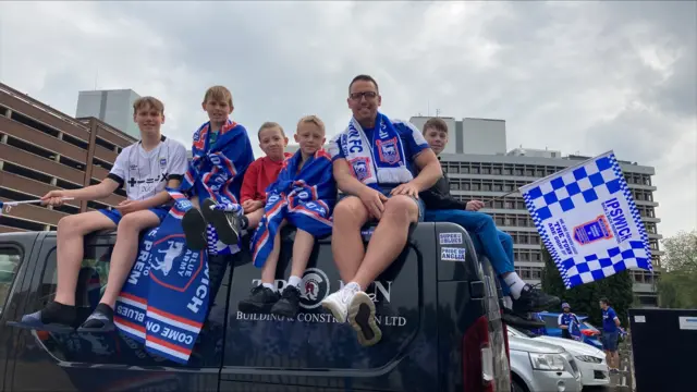 Six people on a van, wearing Ipswich kits and holding flags