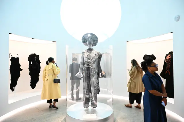 People view dresses and outfits on display in a museum