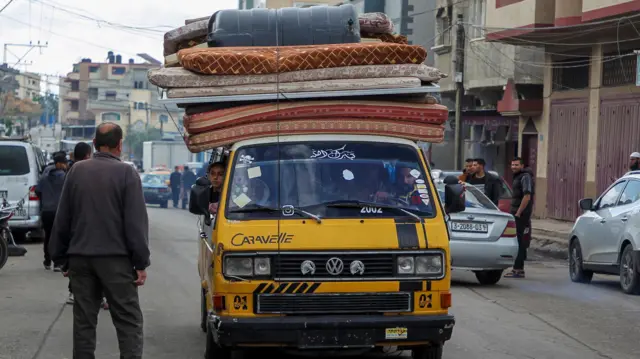 Yellow vehicle with mattresses piled on the roof drives along the road