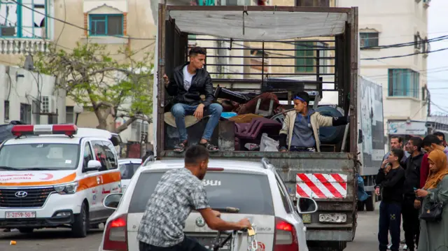 Man and child sit in the back of a truck with items crammed in the back