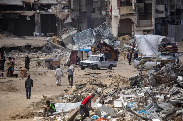 A vehicle carrying two people and their belongings surrounded by damaged homes in the city of Khan Yunis