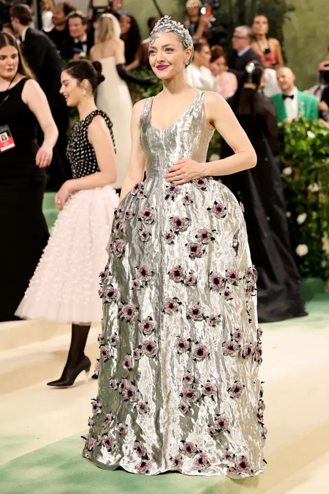 A white woman wears a silver gown covered in beaded pink flowers