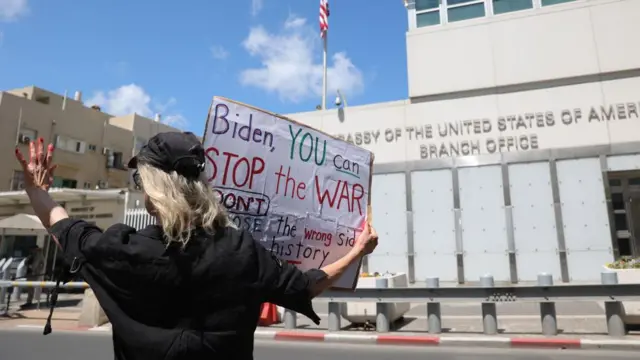 Protester outside US embassy in Tel Aviv, carrying a placard urging Joe Biden to shop the war