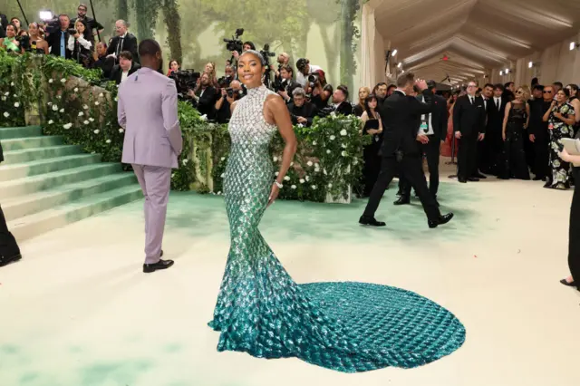 A Black woman wears a gown covered in white, teal and blue sequins