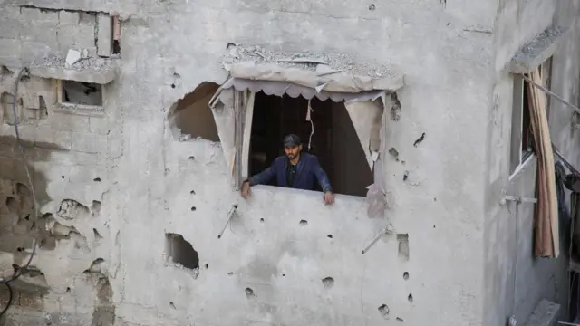 A Palestinian man looks out of a house damaged in an Israeli strike