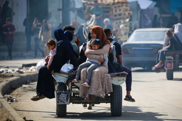 Two women with children on their laps sit on a vehicle carrying about three other people.