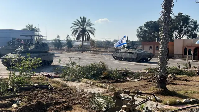 Three tanks, one flying the Israeli flag, are in a carpark.