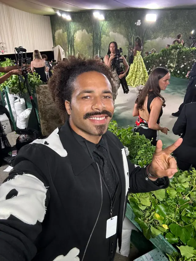 A black man flashes a peace sign on a green carpet