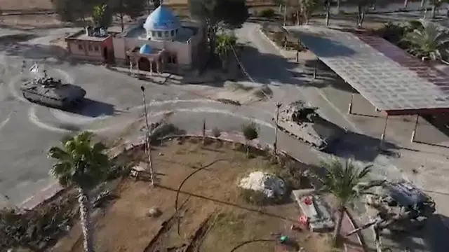 Three tanks, the one in the rear flying the israeli flag, drive along a road