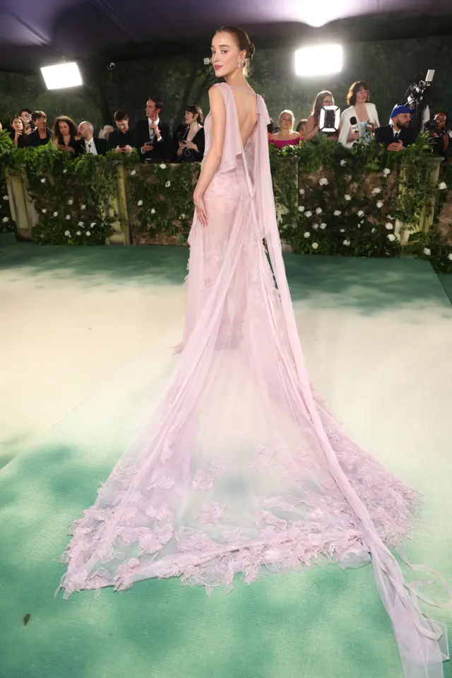 A white woman in a long pastel pink gown made of sheer fabric