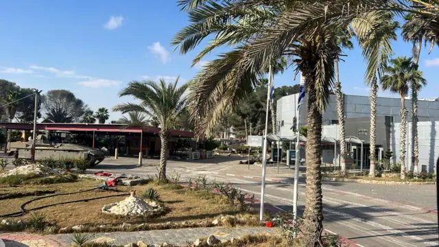 A tank drives along a road by a grey building