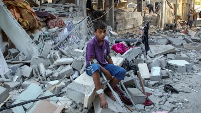 A child with crutches sits on debris at the site of a strike on a house in Rafah.