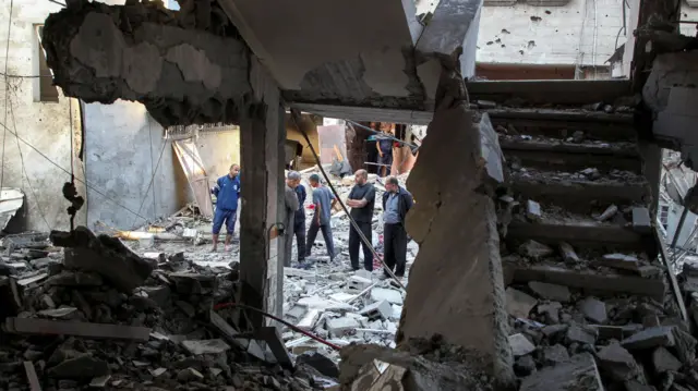 Several Palestinians gather amid debris at the site of a strike on a house in Rafah.