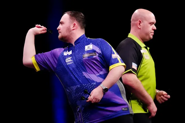 Luke Littler throws as Michael van Gerwen walks back