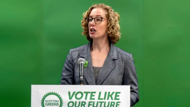 Lorna Slater speaks into a microphone while standing in front of a green background