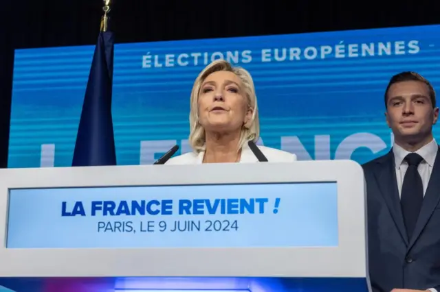 National Rally parliamentary party leader Marine Le Pen delivers a speech standing next to RN president Jordan Bardella