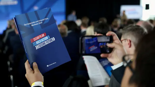 A person takes a photo of the Conservative manifesto at the Tories' launch event