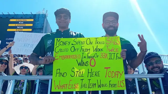 Two Pakistan fans with a sign which says 'money spent on tickets, called off work twice, wins 0 and still here today'