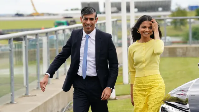 Prime Minister Rishi Sunak and wife Akshata Murty, wearing yellow, arrive in a car at Silverstone