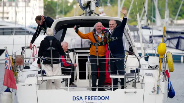 Liberal Democrat leader Sir Ed Davey on a boat waving at the camera with the party's candidate for Torbay Steve Darling Steve Darling, on board