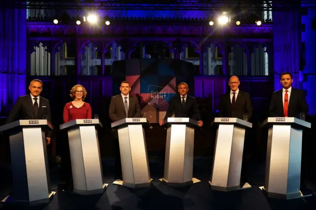 Alex Cole-Hamilton, Lorna Slater, Douglas Ross, presenter Stephen Jardine, John Swinney and Anas Sarwar standing at lecterns for the debate