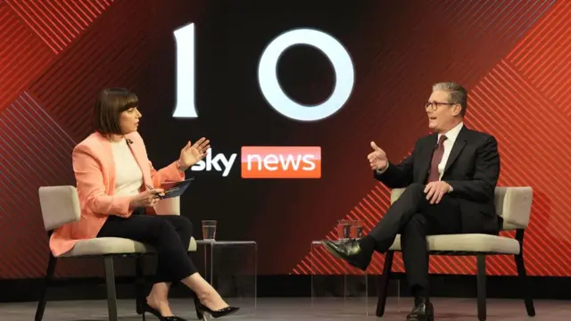 Beth Rigby and Sir Keir Starmer sit in white chairs on a red stage.