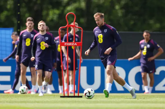 Harry Kane collects the ball in front of a red free-kick mannequin and fellow players