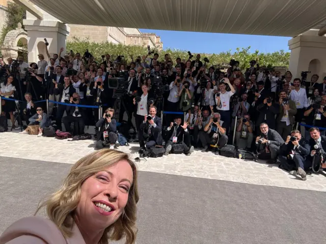 Giorgia Meloni takes a selfie with dozens of journalists gathered behind her