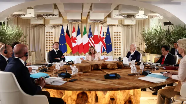 Seven leaders sit round wooden G7 round table