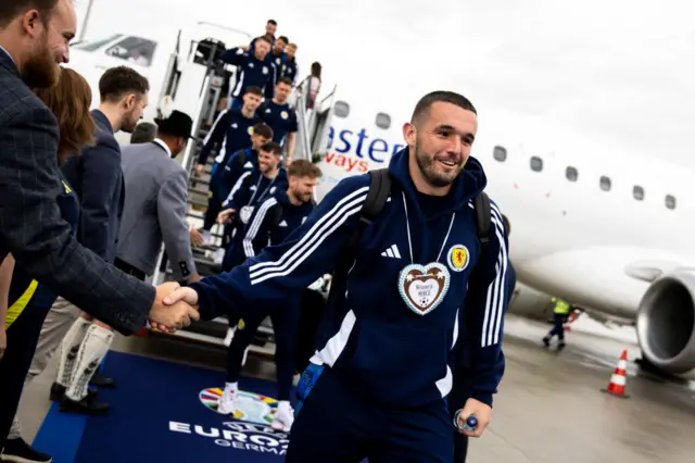 John McGinn shakes hands with someone greeting him as the Scotland squad disembarks the plane which flew them to Germany for Euro 2024