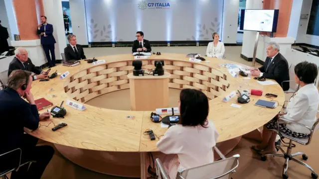 Eight people sit around circular desk at G7