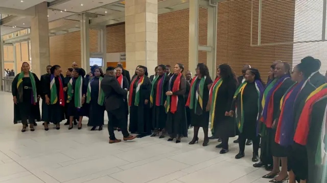 A choir stands in South Africa's parliament with the national flag draped round their necks