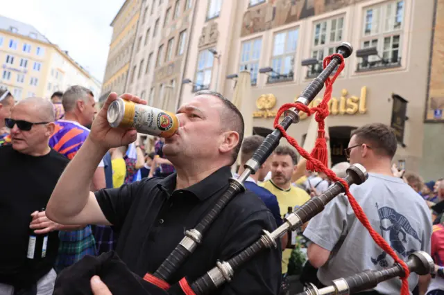 Scotland fan drinks a beer whilst holding a set of bagpipes