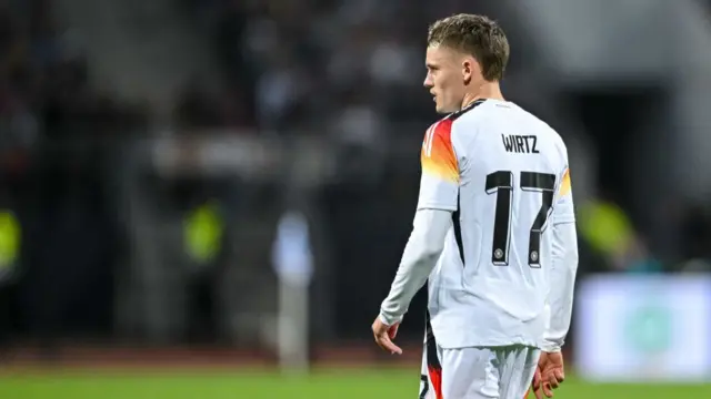 German footballer Florian Wirtz standing with his back to the camera dispalying the number 17.  He is wearing a white germany top whilst playing a football match