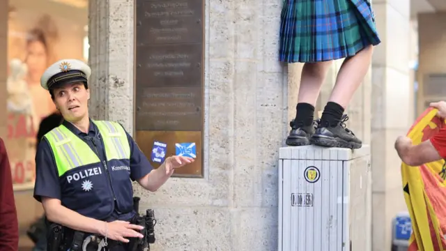 A female police officer looks towards the legs of a Scotland fan wearing a kilt ahead of UEFA EURO 2024