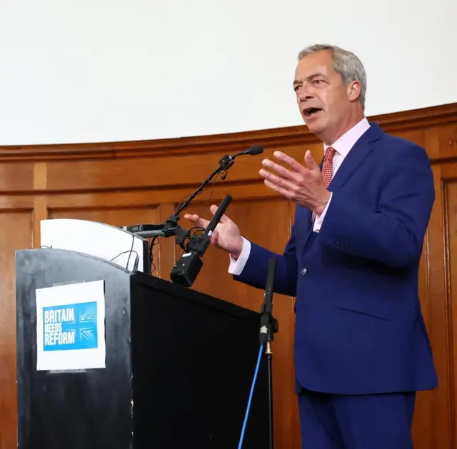 Reform UK leader Nigel Farage standing behind a black lectern with a sign with the words Britain needs reform. His hands are animated as he talks