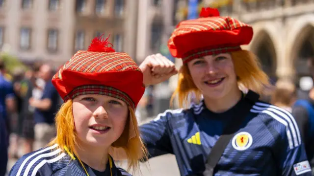 Two young scotland fans in Germany. Both are wearing tartan hats and Scotland football tops. They are both smiling to the camera