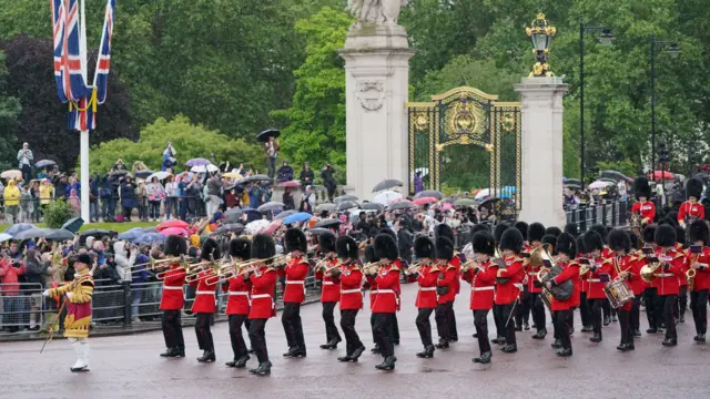 Military band walking as people sheltering under umbrellas look on