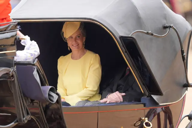 The Duchess of Edinburgh, dressed in yellow, travels in an open carriage