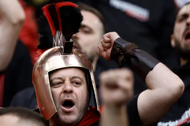 An Albania fan roars support from the stand wearing a roman helmet