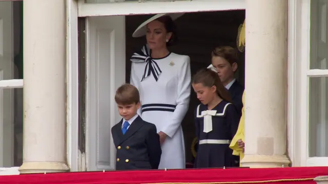 Catherine stands in a balcony with her three children.