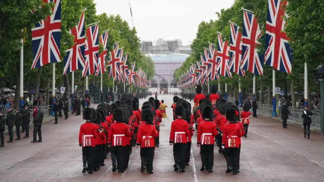 Troops in red walk down The Mall, with Union Jacks flying alongside