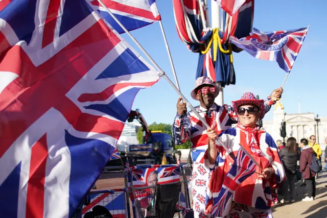 Two royal fans dressed in clothing featuring England flags and waving more flags