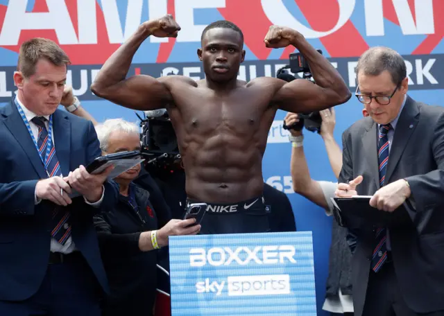 Ezra Arenyeka stands on the scales with his arms raised in the air