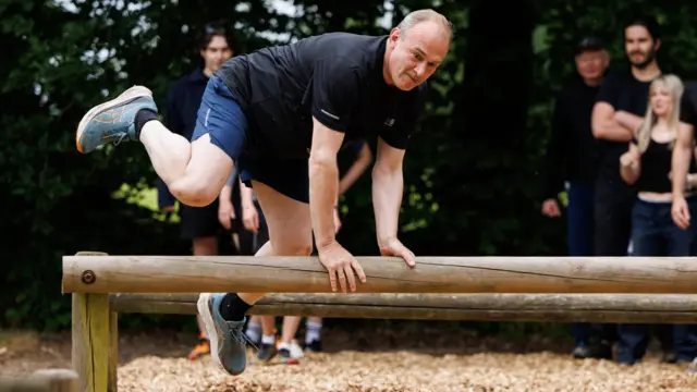 Ed Davey vaulting a wooden pole