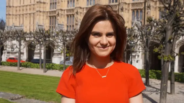 Jo Cox wearing a red dress outside the Houses of Parliament