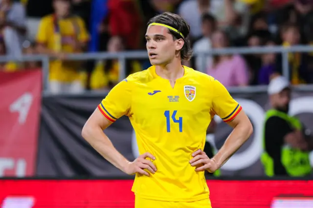 Romanian midfielder Inais Hagi standing with his hands on his hips.  He has a tired look on his face whilst playing internationally for Romania.  He is wearing a yellow strip with a blue number 14.