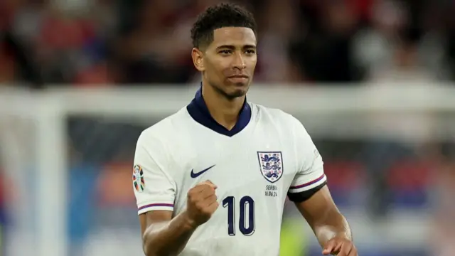England Midfielder Jude Bellingham celebrating an England goal with a clenched fist.  He's wearing a white England top with the number 10 on the front.